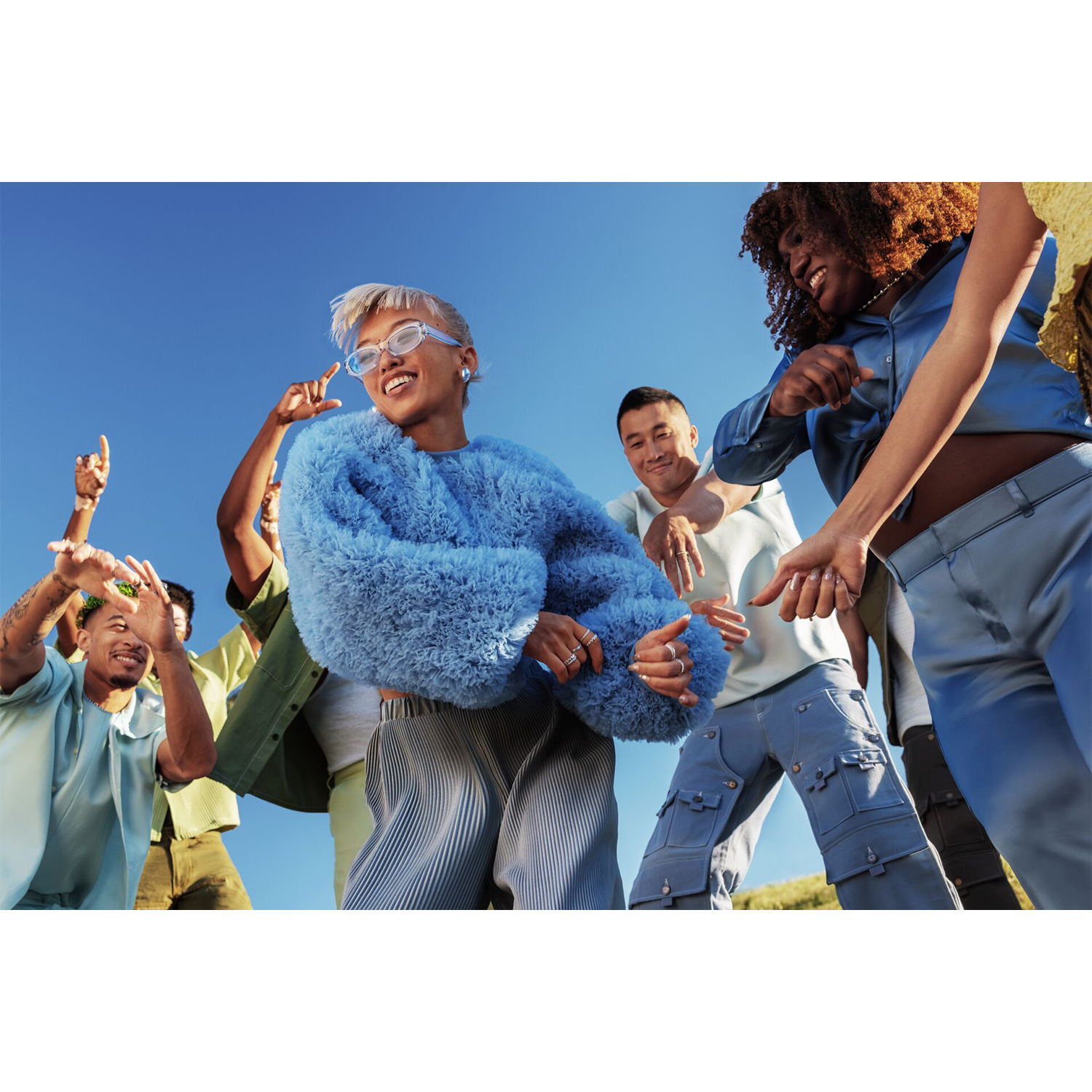 Un gruppo di persone che ballano all'aperto sotto un cielo blu. Sono di diverse etnie.