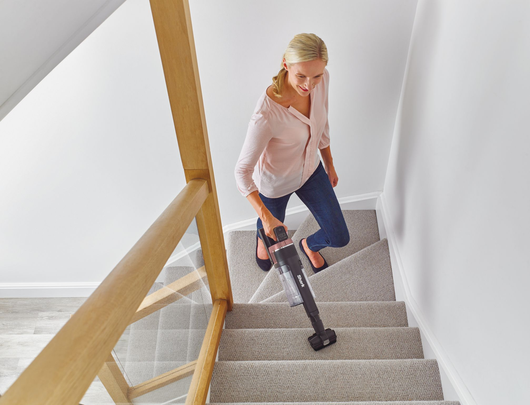 Une femme utilisant un aspirateur à main, nettoyant un escalier en moquette.