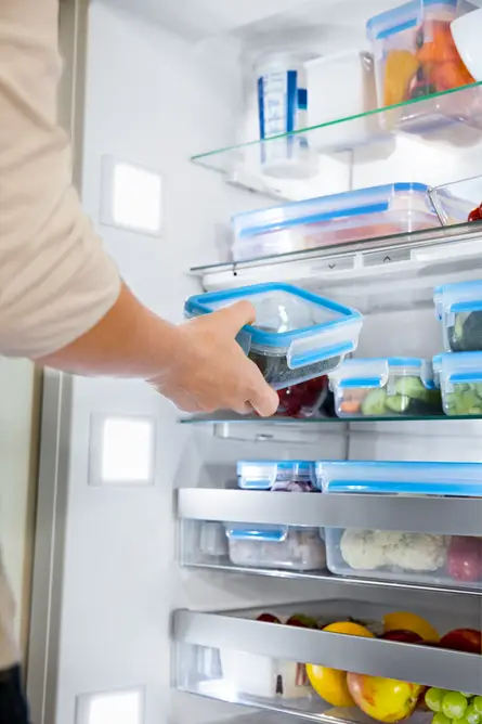 Osoba wkładająca niebieski pojemnik z jedzeniem do lodówki.