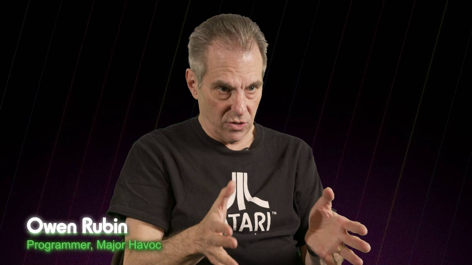 Hombre con pelo gris con una camiseta negra de Atari, gesticulando con las manos.