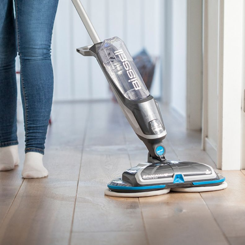 Personne nettoyant un plancher en bois franc avec une vadrouille rotative blanche et grise.