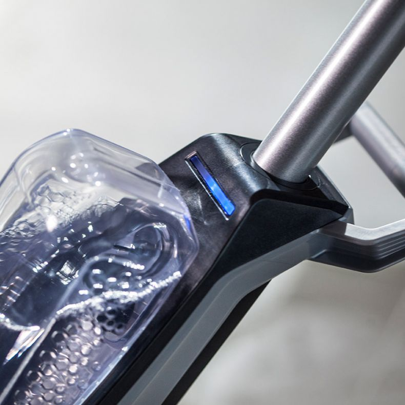 Gros plan sur la poignée d'un aspirateur, un réservoir d'eau transparent et un indicateur lumineux bleu.