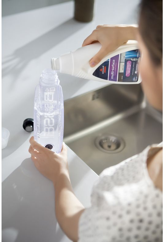 Une personne verse du liquide de nettoyage d'une bouteille dans une bouteille de nettoyage à l'intérieur d'un évier.