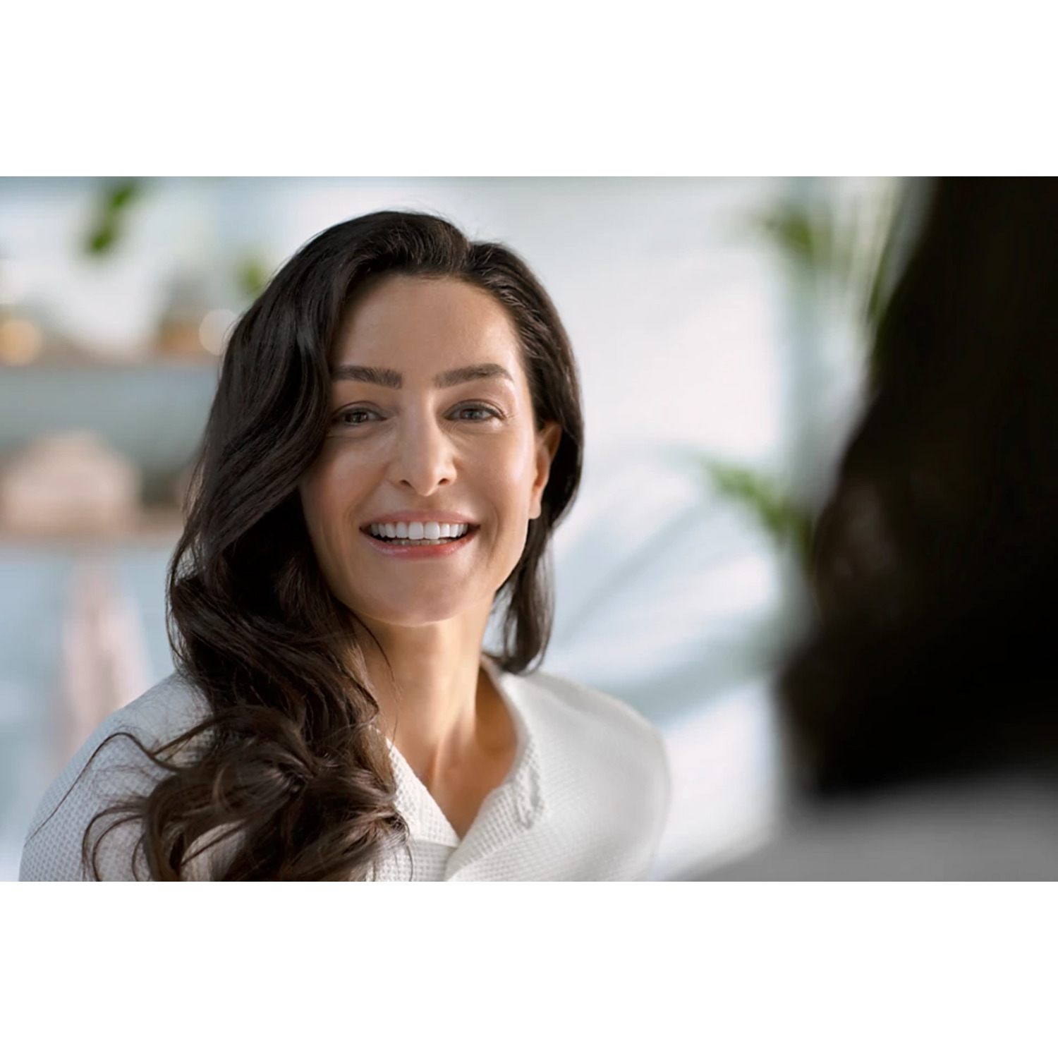 A woman smiles at the camera. She has dark hair and a white robe.