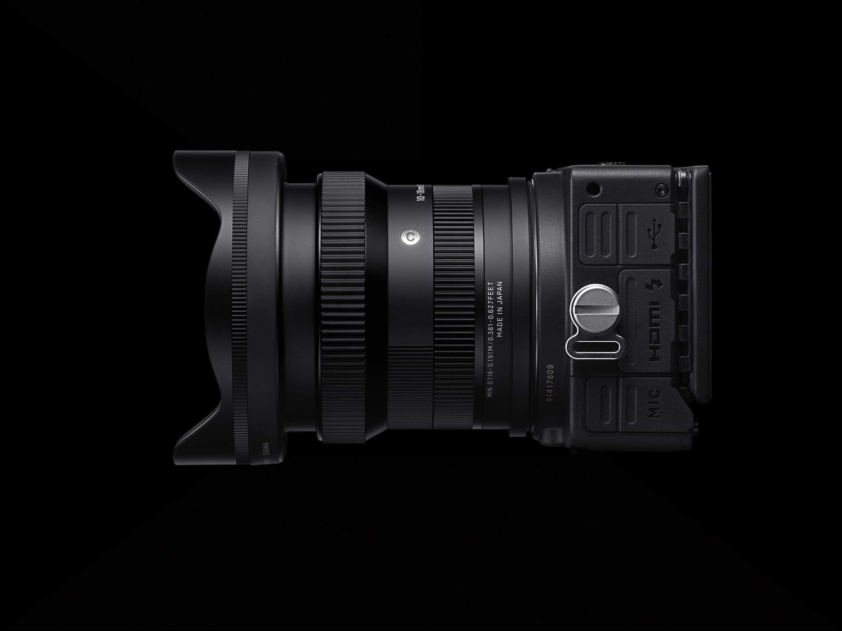 Schwarzes Kameraobjektiv an einem Kameragehäuse vor schwarzem Hintergrund.