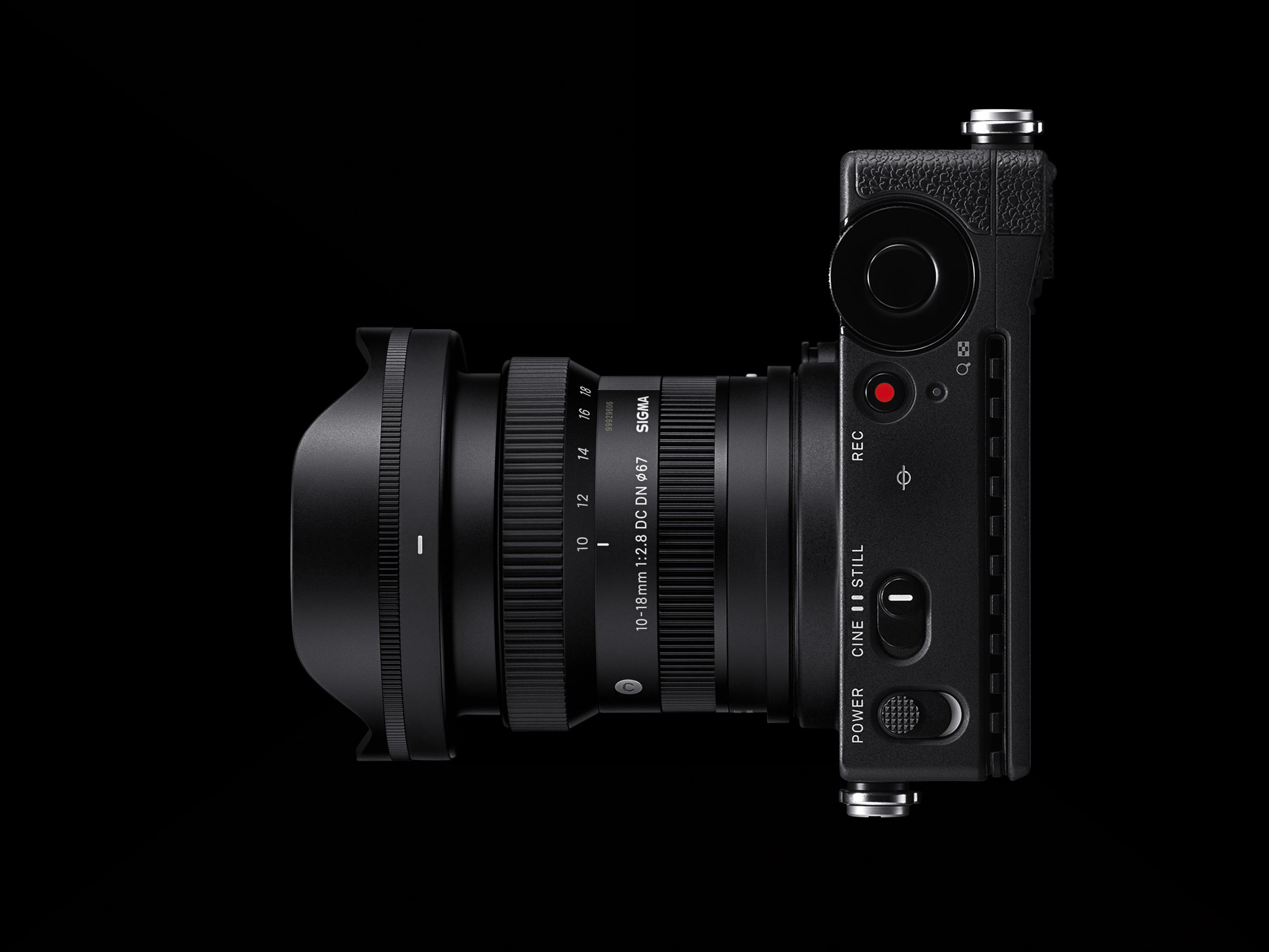 Schwarze Kamera mit Objektiv. Das Objektiv ist mit SIGMA 10-18mm beschriftet. Die Kamera liegt auf schwarzem Grund.