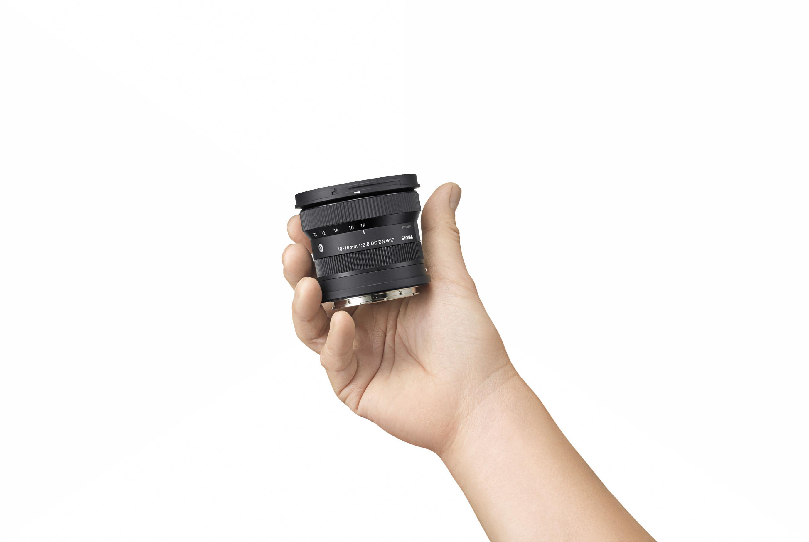 Person hält ein schwarzes Kameraobjektiv, weißer Hintergrund. Objektiv mit Text und Markierungen.