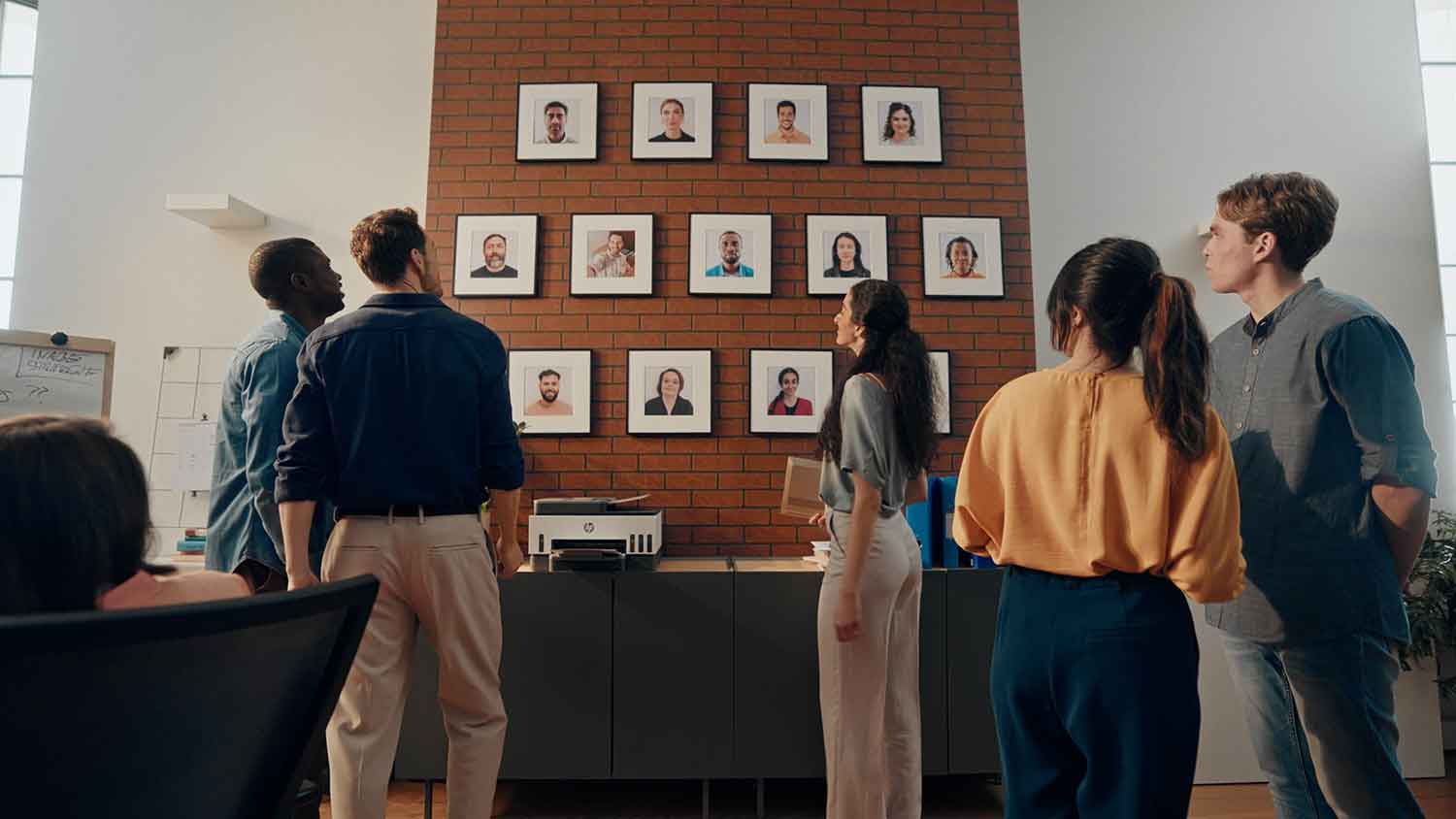Groep mensen die naar foto's op een bakstenen muur kijken. Sommigen kijken naar de foto's.