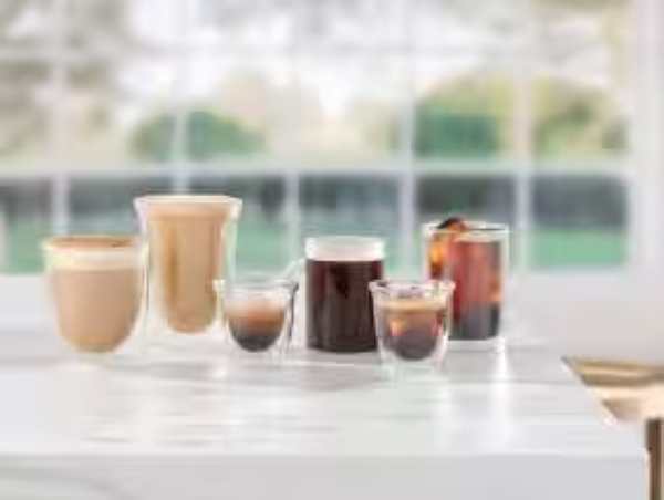 Różne napoje kawowe w przezroczystych szklankach na białym stole z rozmytym tłem.