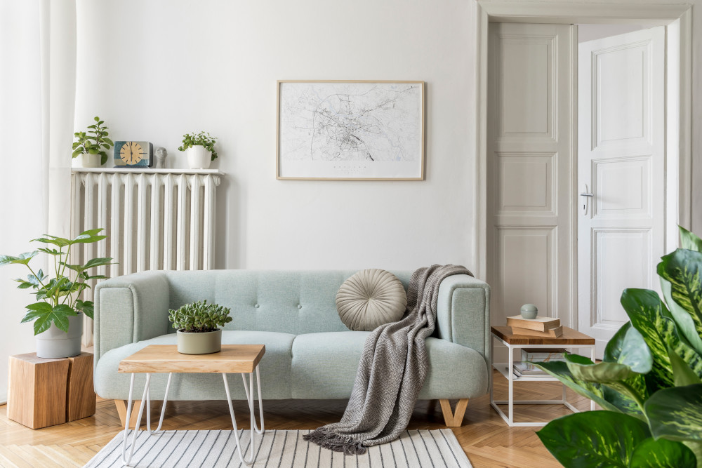 A living room with a sofa, plants, side tables, and a framed picture.