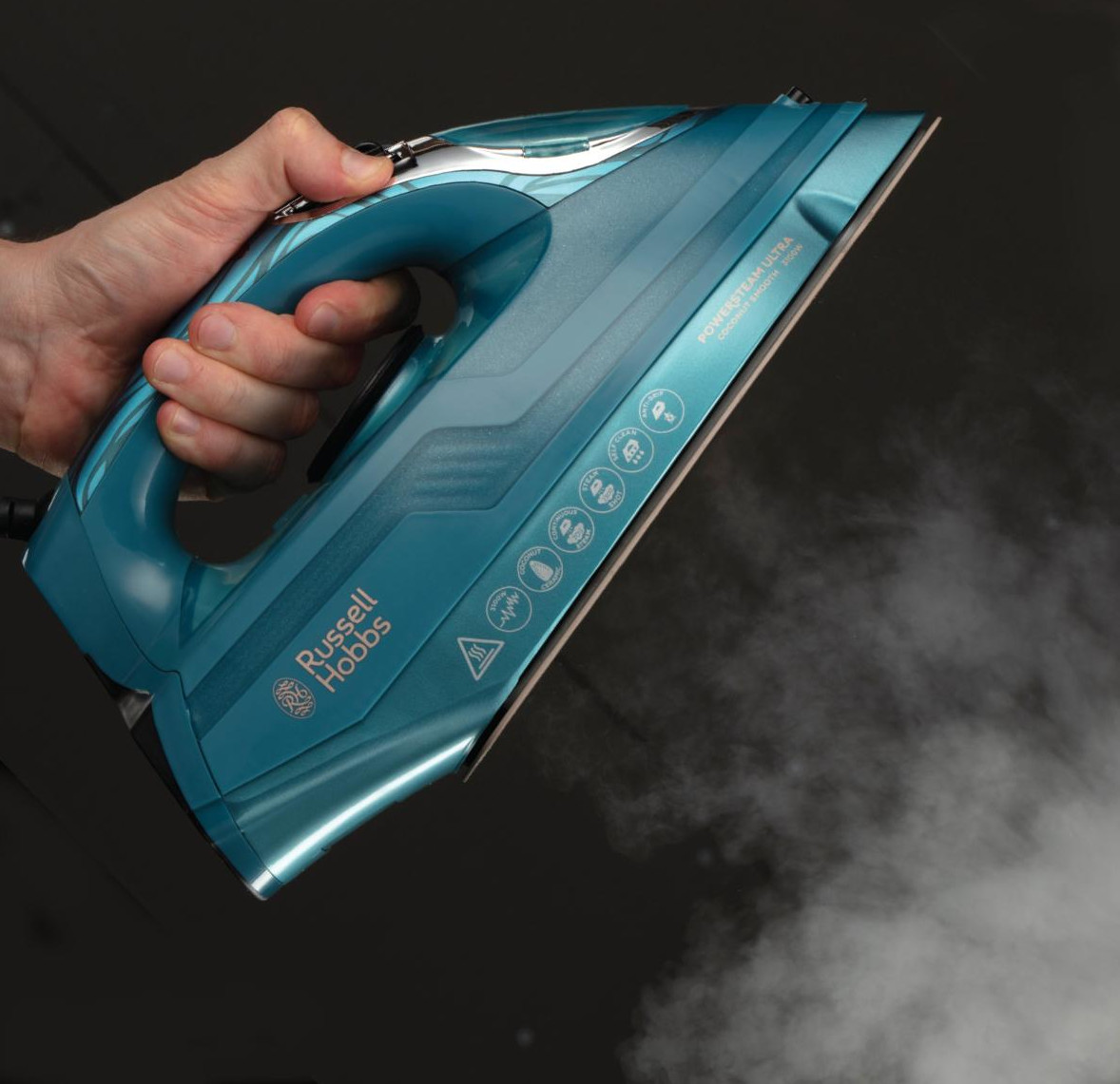 Ręka trzyma niebieskie żelazko. Para ucieka, tło jest ciemne.