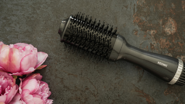 Black hair dryer brush with pink flowers on a dark surface. Koenic is the brand.