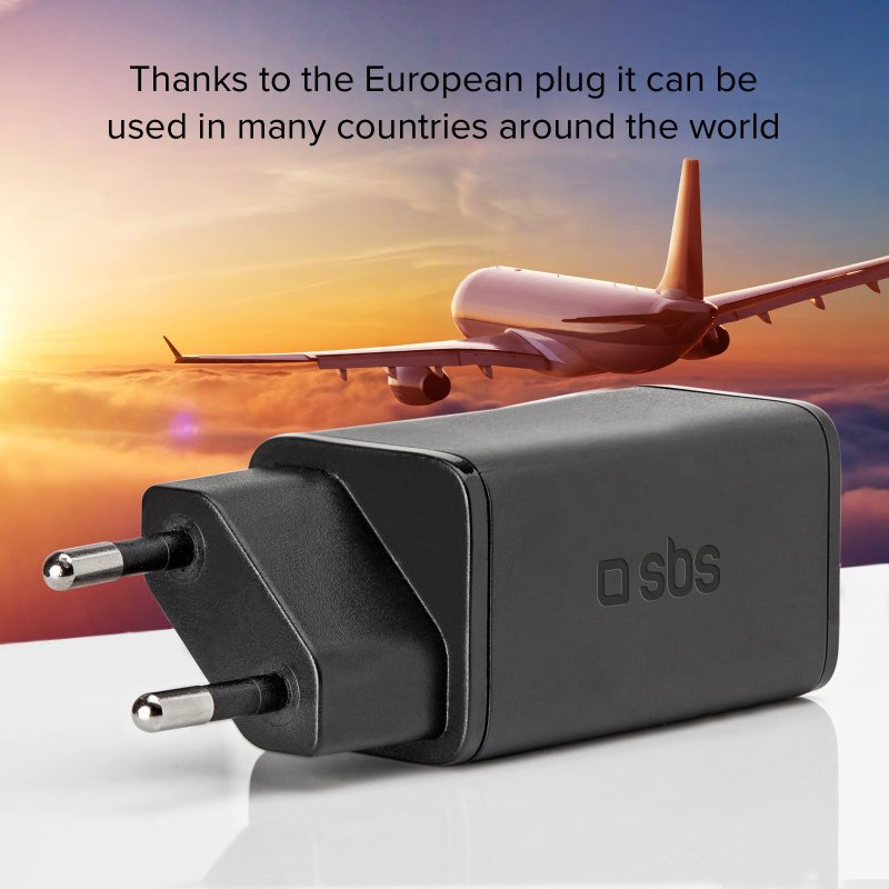 Schwarzer Adapterstecker mit silbernen Stiften, mit Flugzeug im Hintergrund und Text 'sbs'.