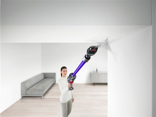 Mujer aspirando un techo con una Dyson. La habitación tiene un sofá y paredes blancas.