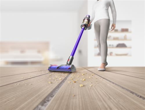 Una mujer aspira un suelo de madera con una aspiradora inalámbrica morada y plateada.