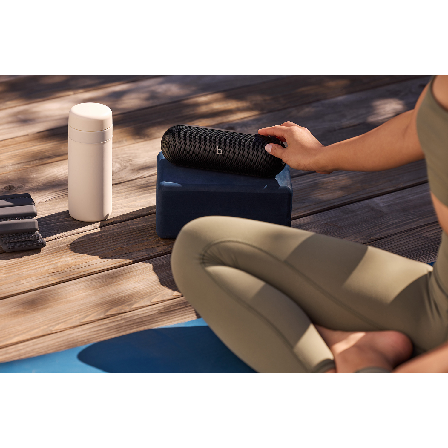 Una donna seduta su un tappetino da yoga raggiunge un altoparlante nero su un blocco blu navy.