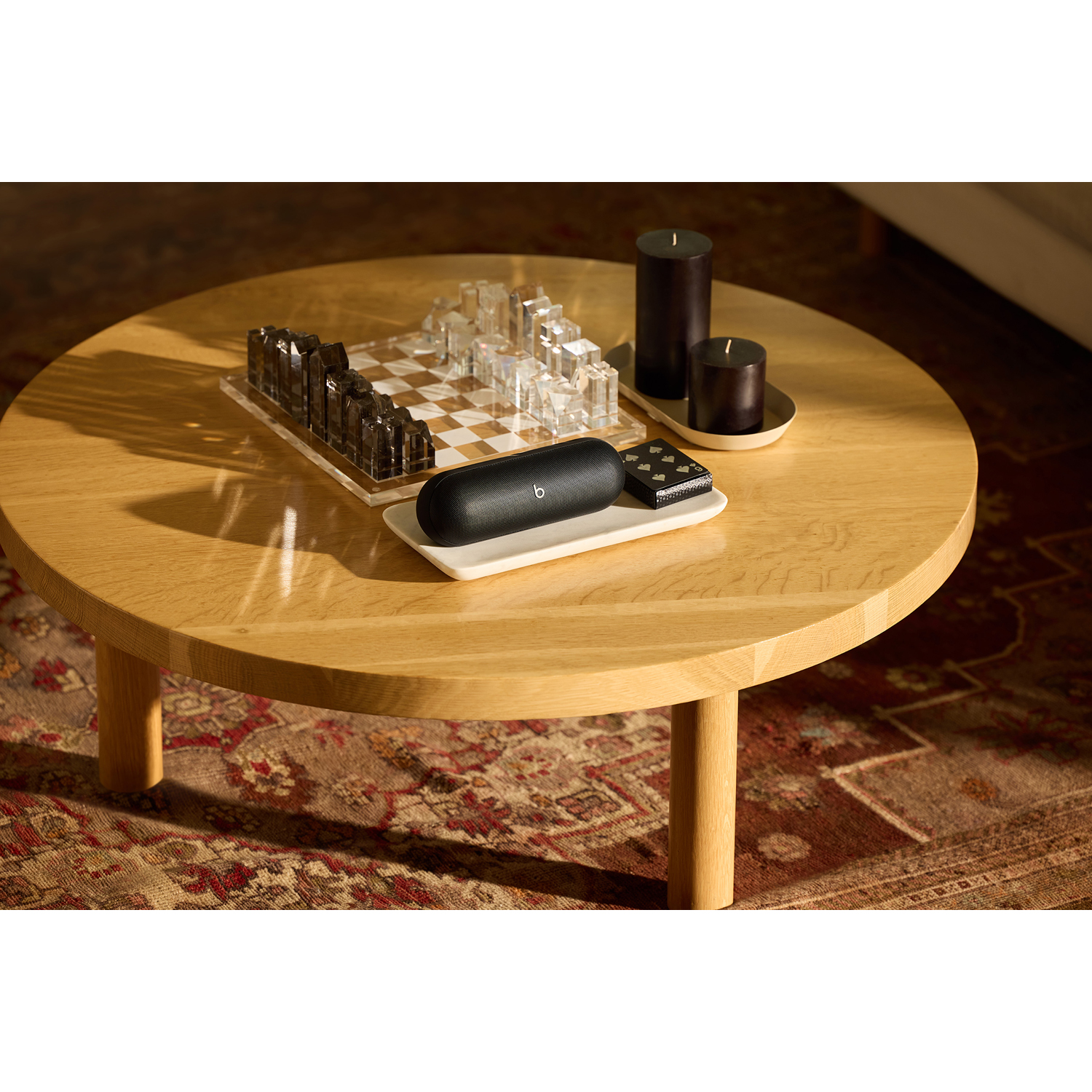 Un tavolino rotondo in legno con scacchiera, candele e un altoparlante Beats.