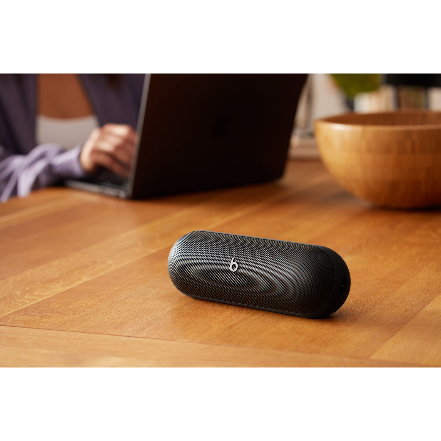 Altoparlante Beats nero su un tavolo di legno, con una persona che usa un laptop sullo sfondo.