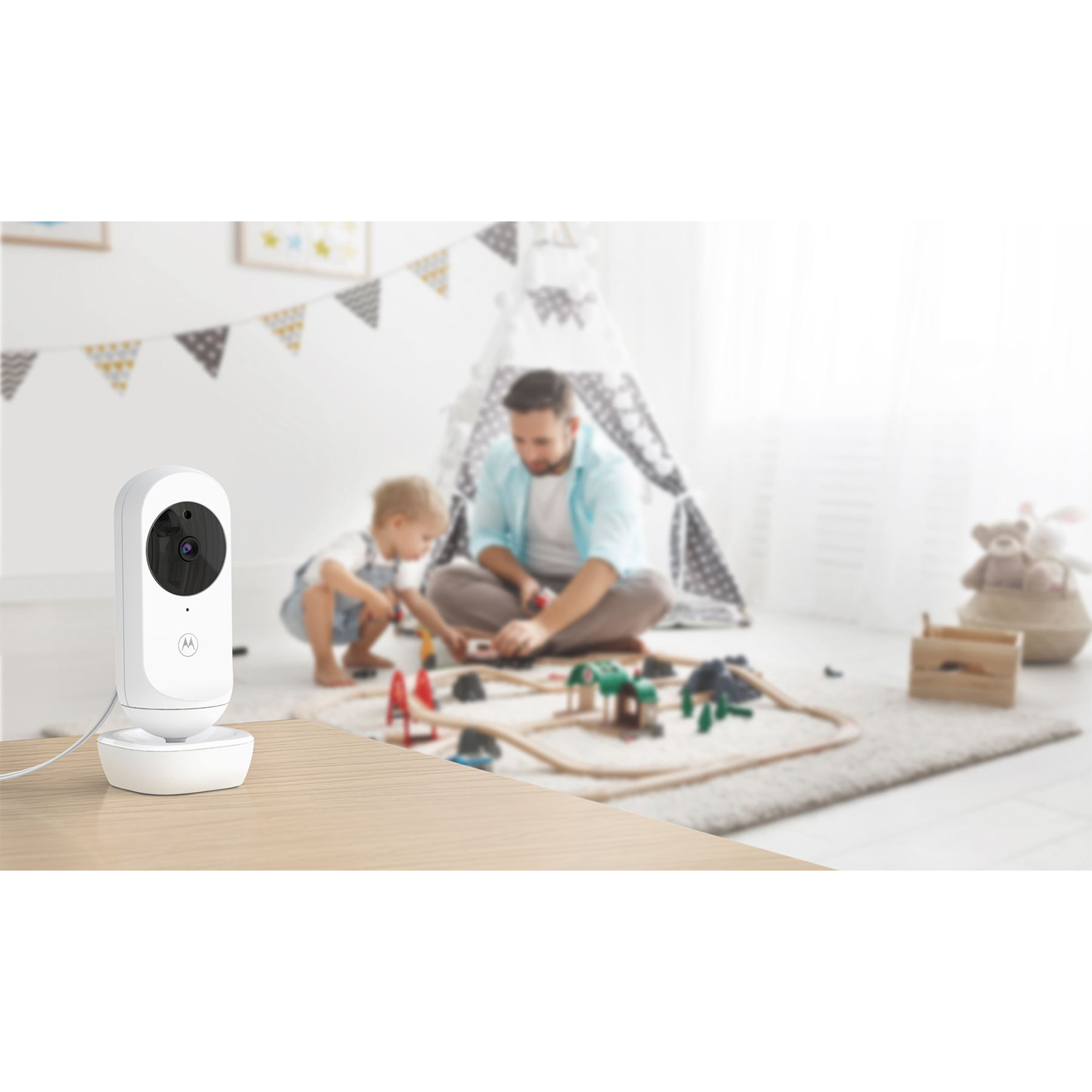 Un baby monitor su un tavolo, con una famiglia che gioca sullo sfondo.