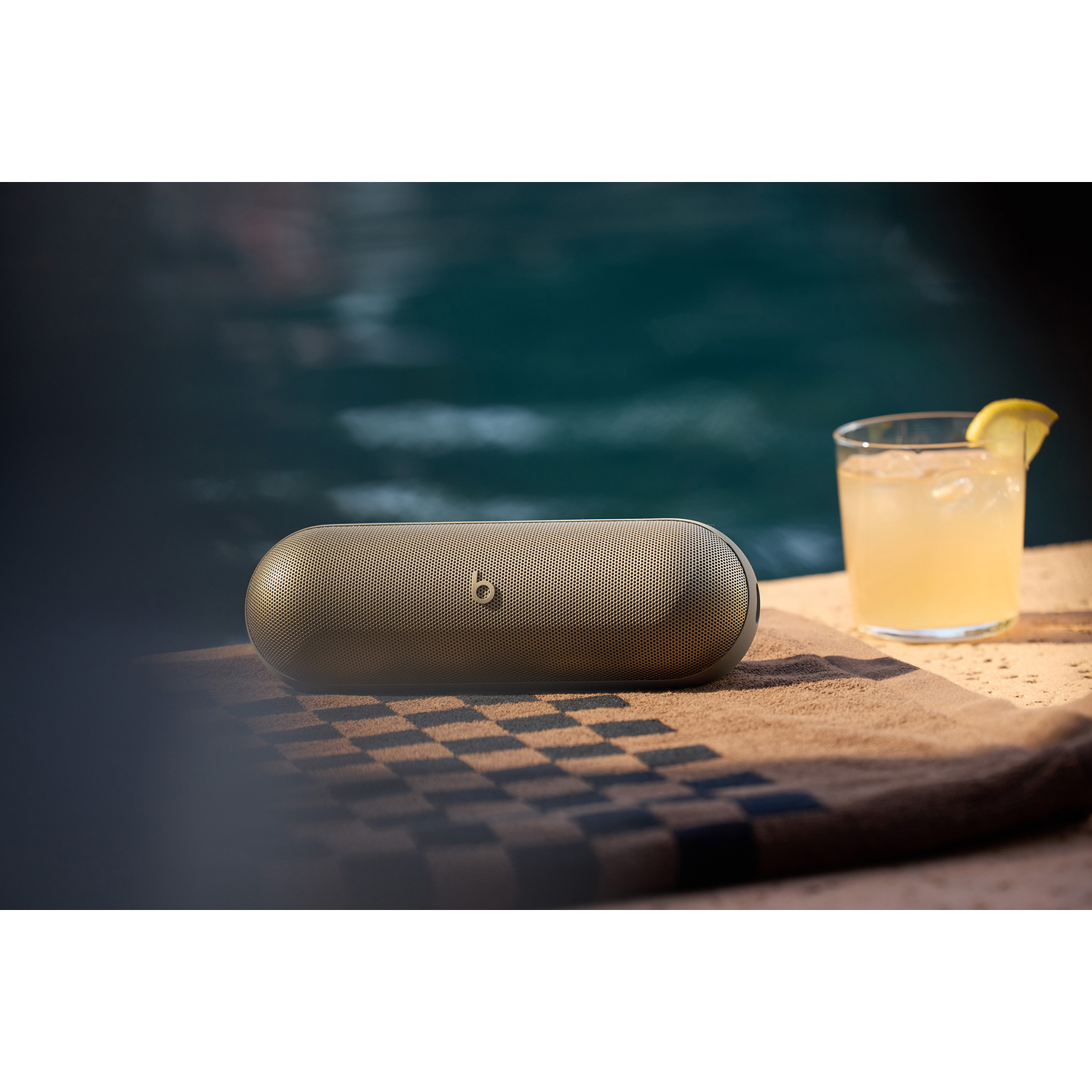 Altoparlante Beats su un asciugamano vicino a una piscina con un drink al limone.