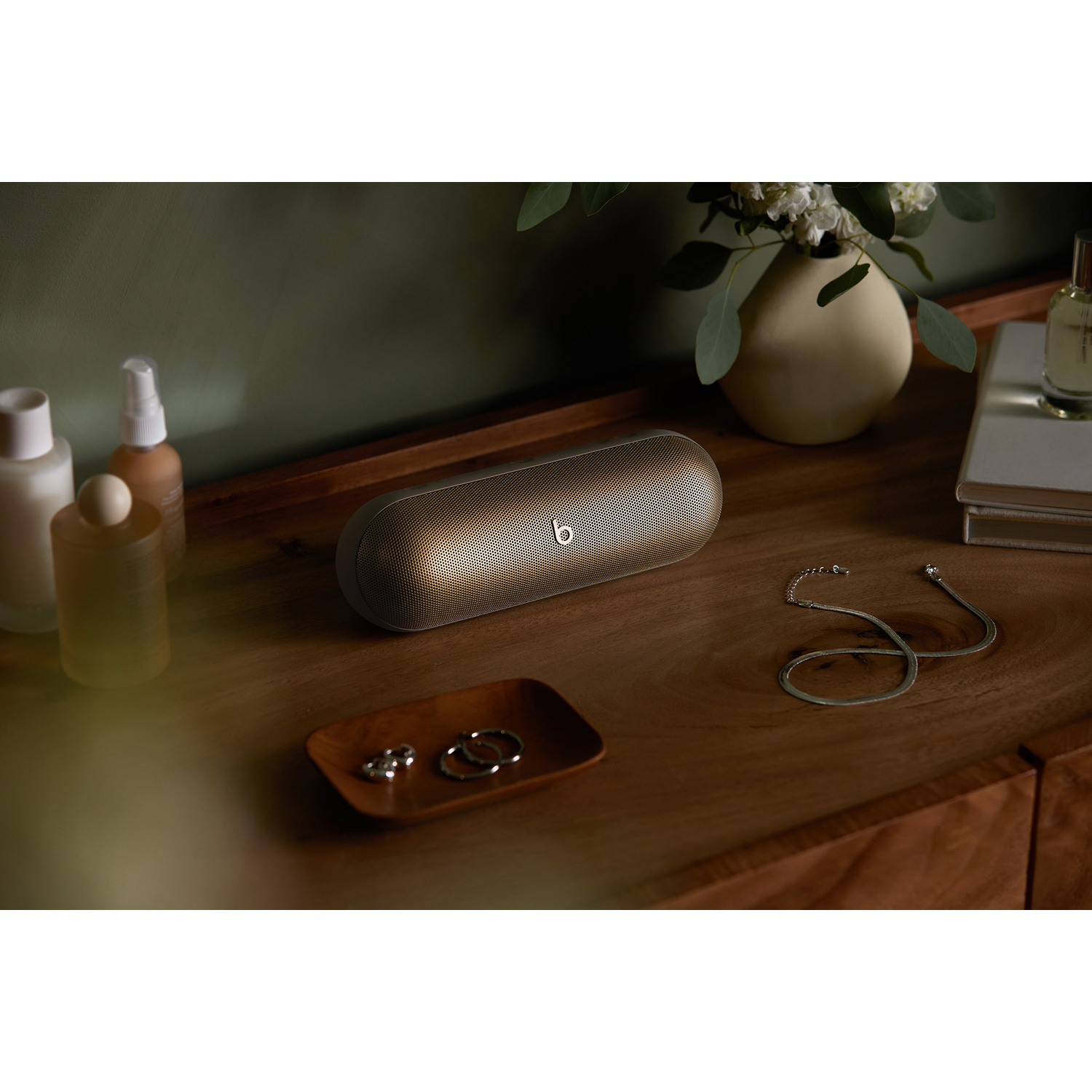 Altoparlante Beats su un tavolo di legno con accessori. Vaso e profumi sullo sfondo.