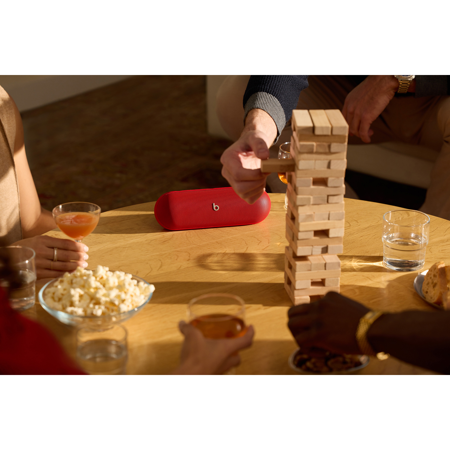 Gruppo che gioca a Jenga, altoparlante Beats rosso sul tavolo. Bevande, snack e persone.