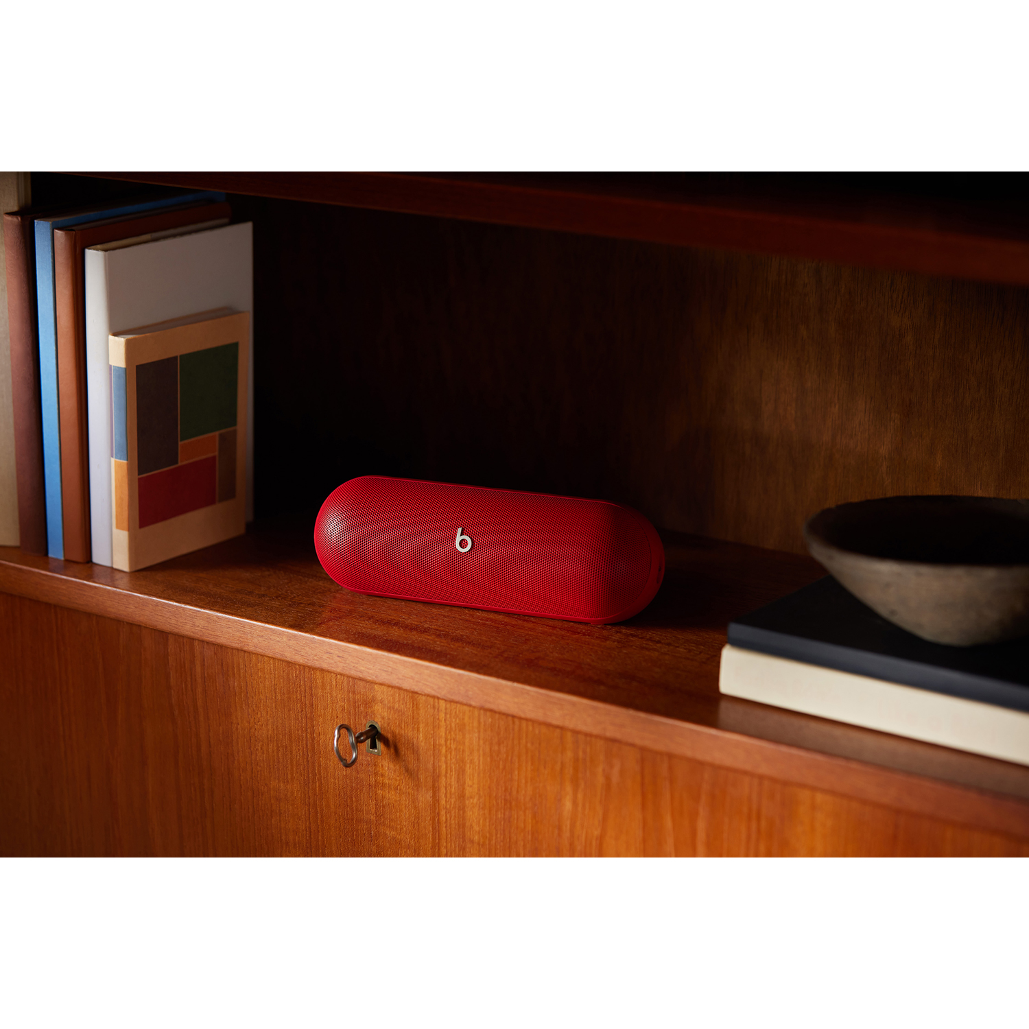 Altoparlante Beats rosso su uno scaffale di legno con libri.