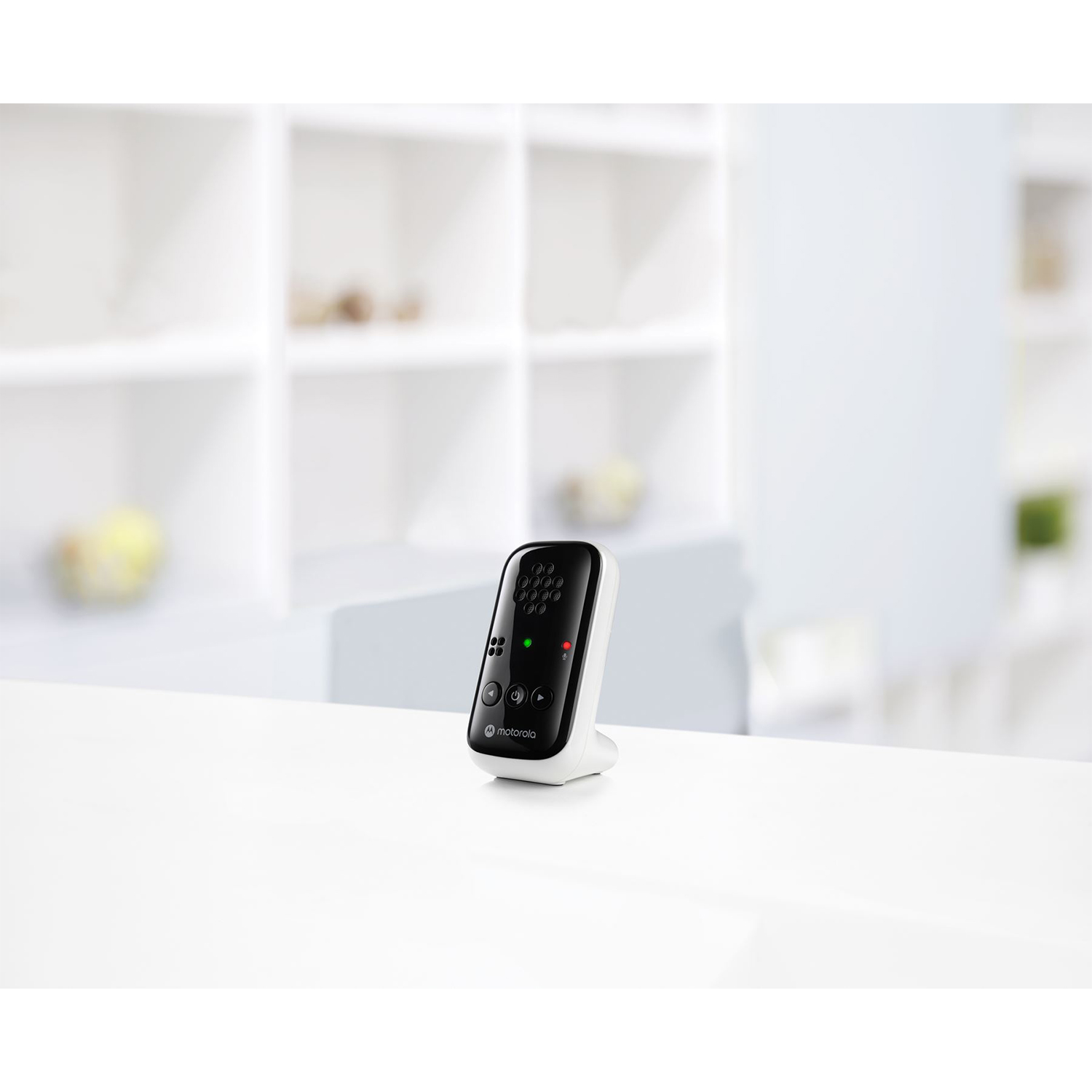 Un baby monitor bianco con display nero. È su un tavolo bianco in una stanza con mensole bianche e un muro bianco.