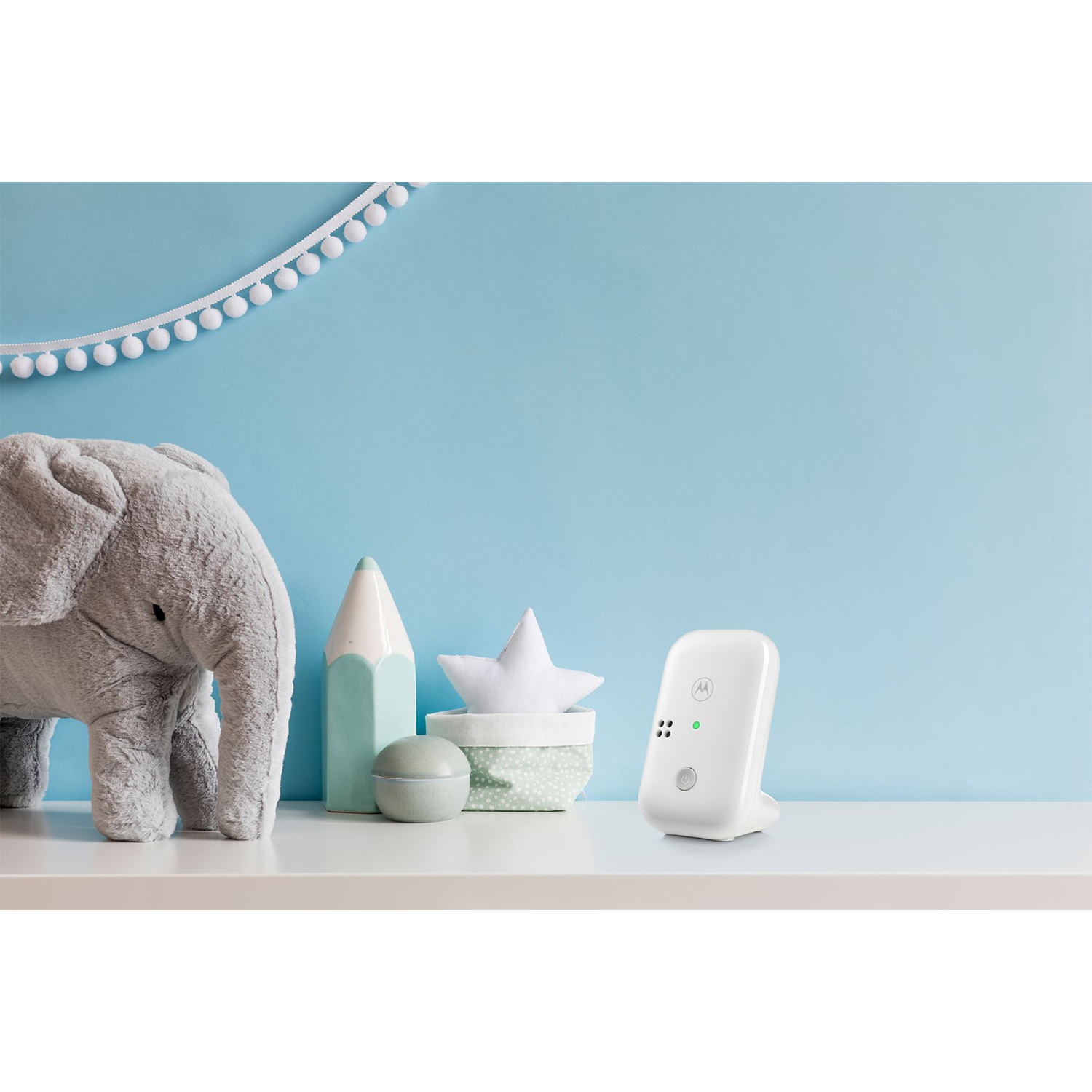 Baby monitor su una mensola bianca con giocattoli, muro blu.