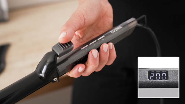 Hand holding a curling iron. The display shows the temperature 200. The tool is black.