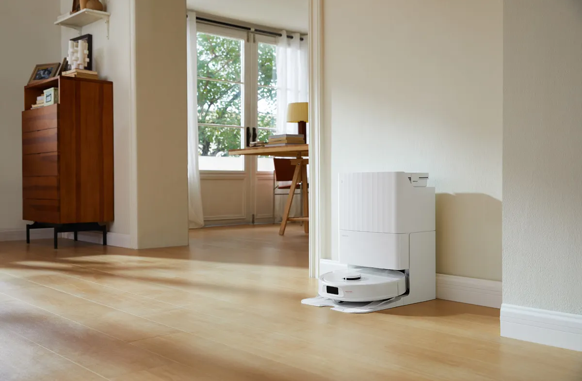 Aspirateur robot dans une station d'accueil sur un plancher en bois. Murs blancs et une porte en arrière-plan.