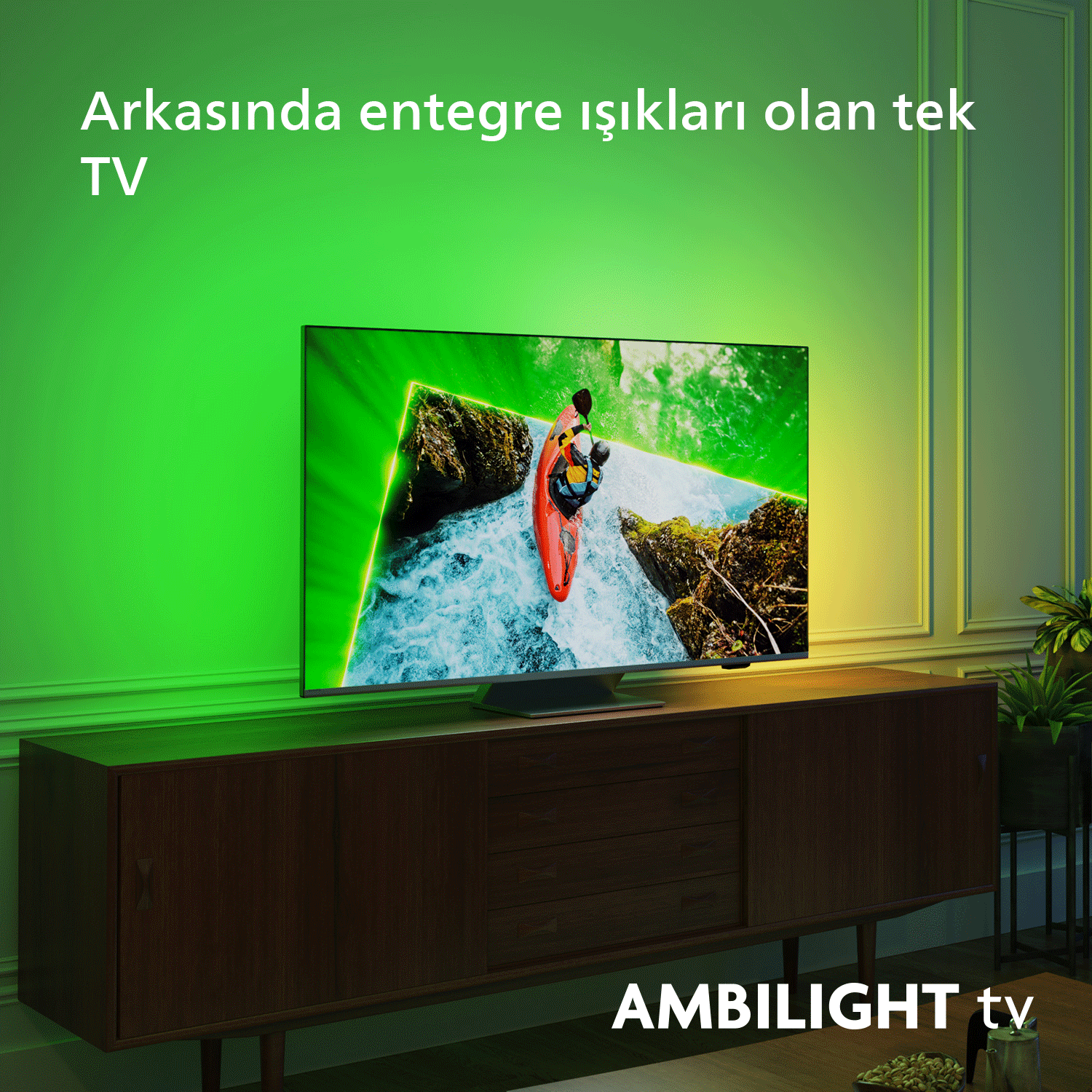 Ahşap dolap üzerinde TV, yeşil ambiyans ışığıyla. Ekranda nehir sahnesi.