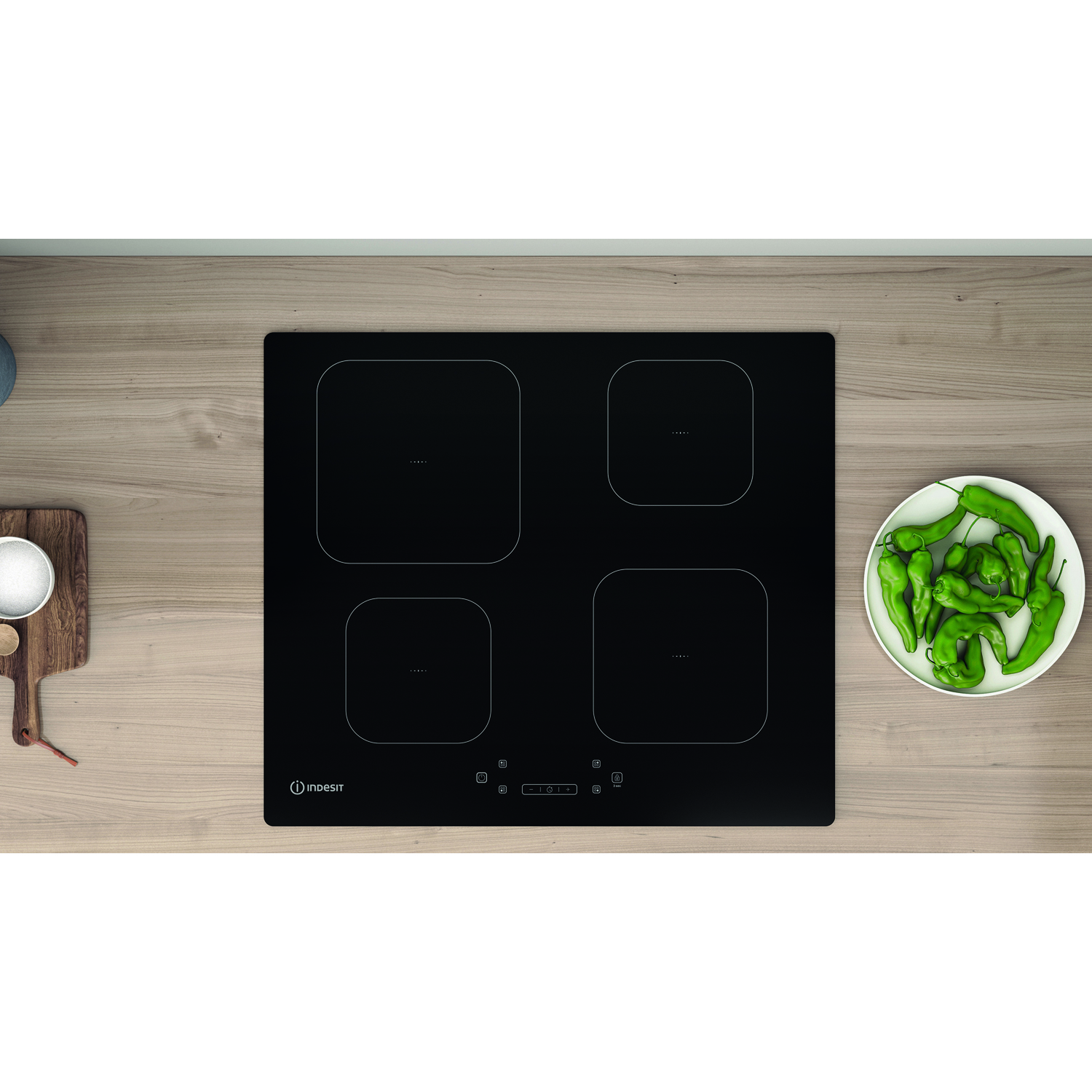 Piano cottura a induzione nero con quattro zone cottura. Piatto di peperoni verdi su legno.