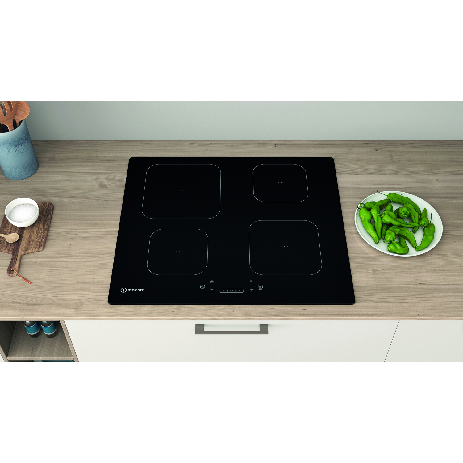 Un piano cottura a induzione nero con quattro zone cottura. Alcuni peperoni verdi su un piatto.