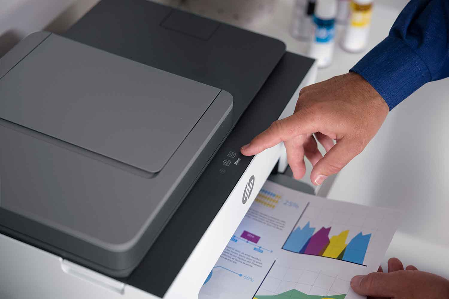 A hand pressing a button on a grey and black printer. A graph with data is visible.