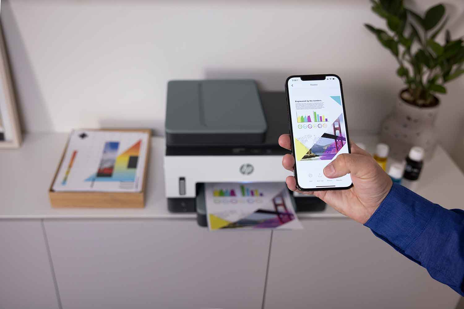 A person holding a phone showing a print job with a printer nearby.