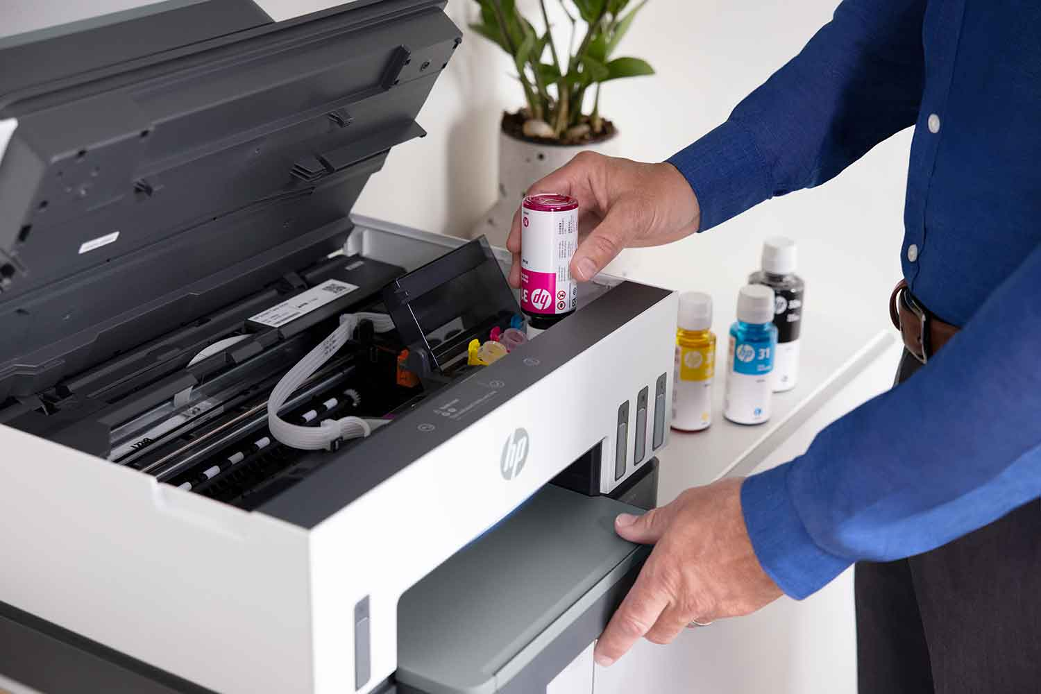 Person filling a printer with ink cartridges. Printer is open, with ink bottles nearby.