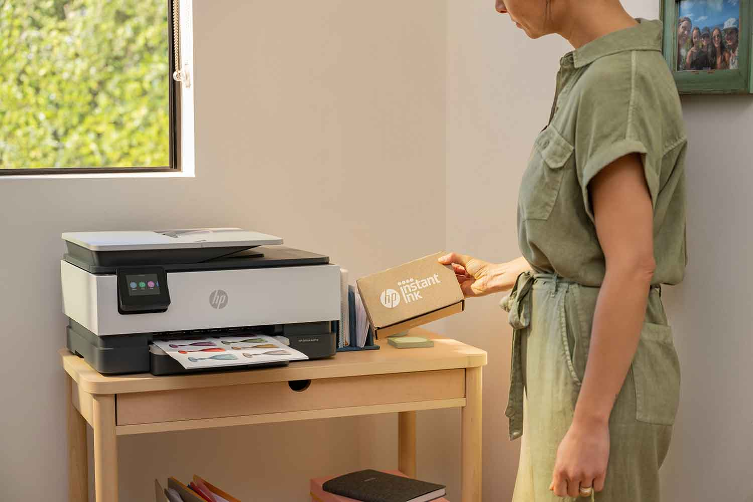 Woman near a printer, holding a box of instant ink.