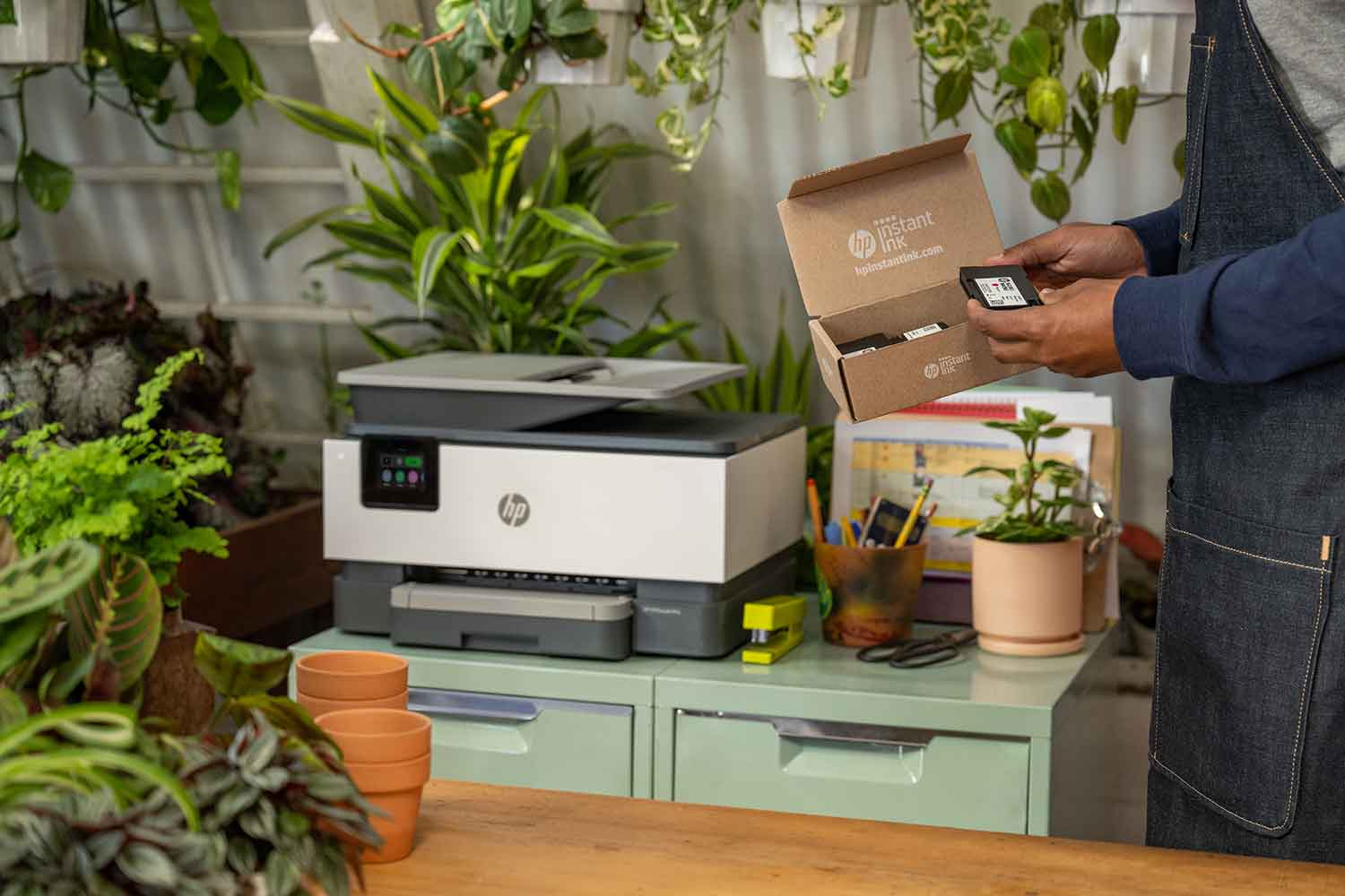 A person opening a box of ink cartridges next to a printer.