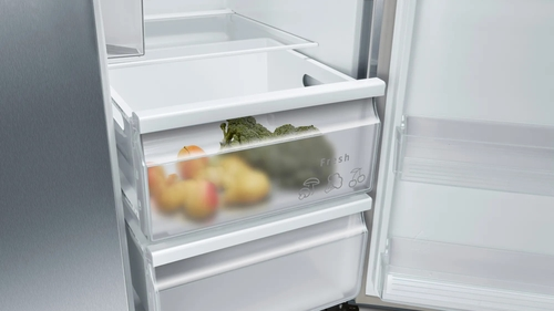 Refrigerador abierto con productos frescos en cajones. Manzanas, brócoli y verduras.