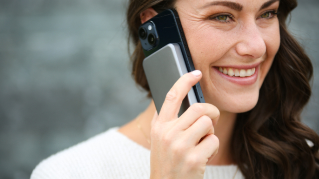 Mujer sosteniendo un teléfono junto a su oreja. Una batería externa está adherida a la parte trasera del teléfono.