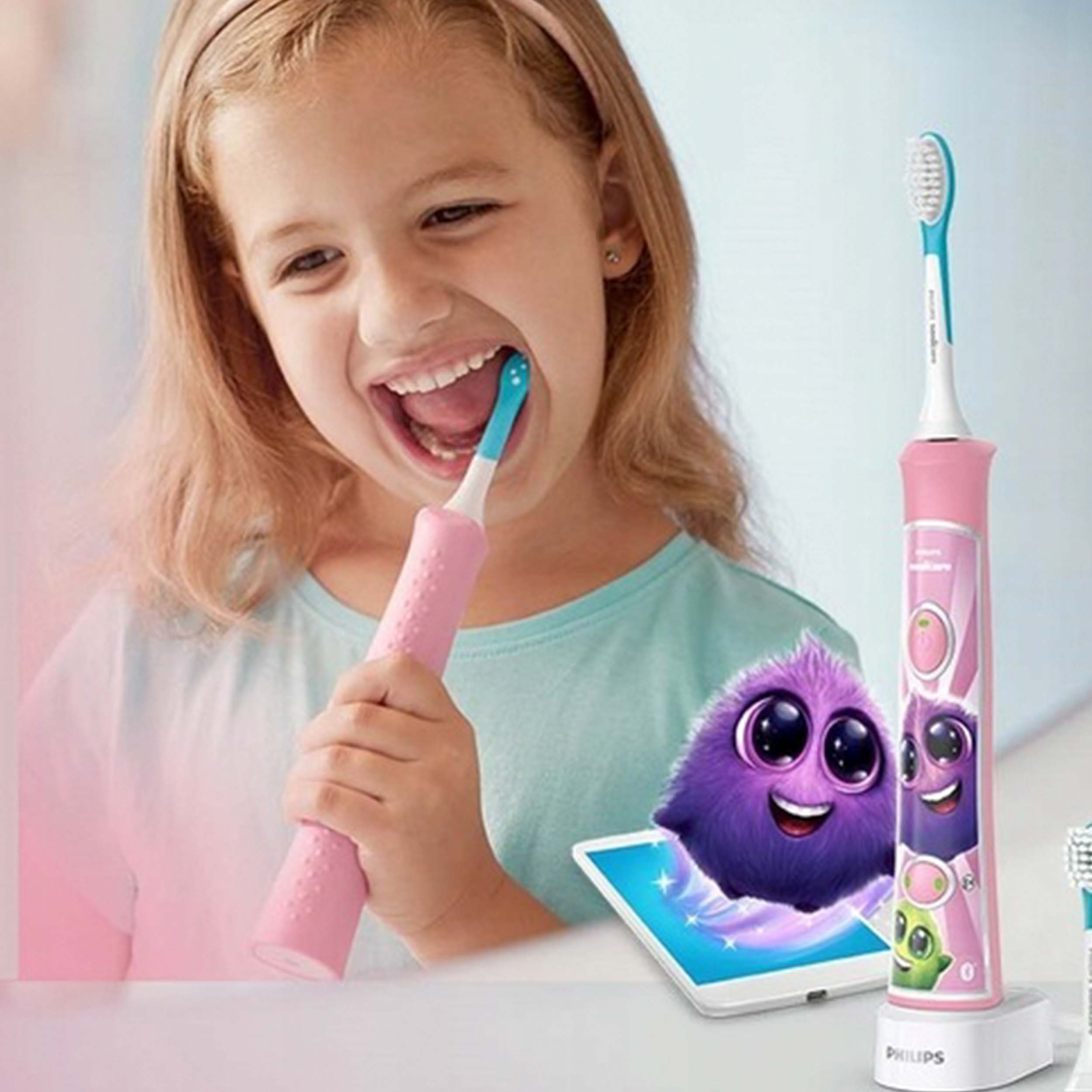 Dziewczynka szczotkująca zęby różową szczoteczką. Kreskówka na stole. Stacja ładująca na dole.