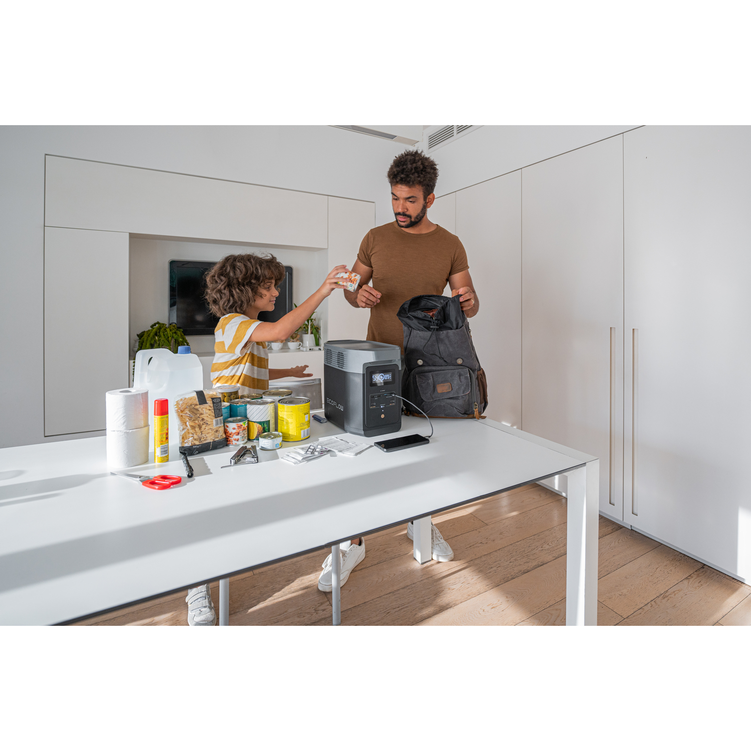 Man en kind bereiden spullen voor, met een powerstation op een tafel.