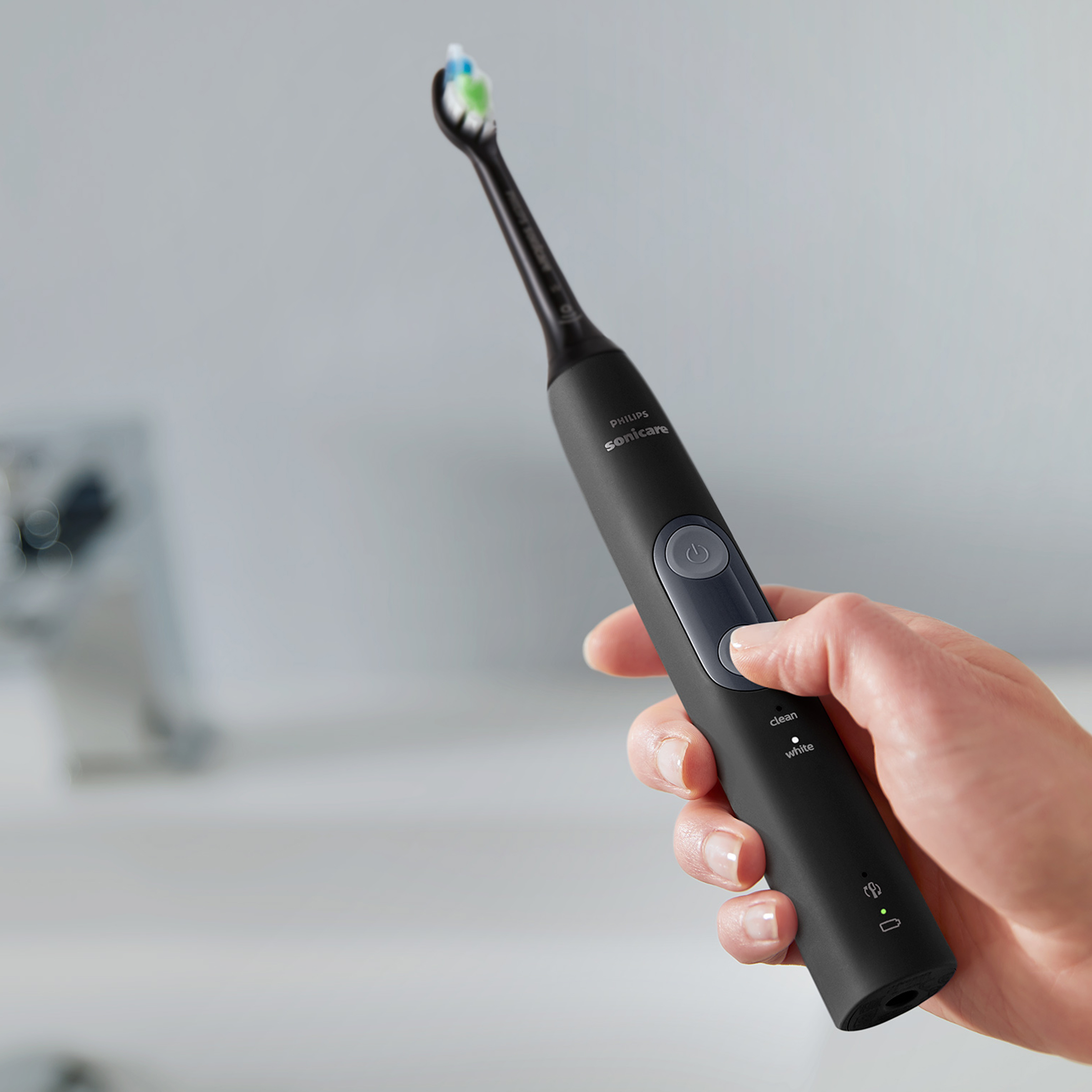 Czarna elektryczna szczoteczka do zębów w dłoni. Szare tło.
