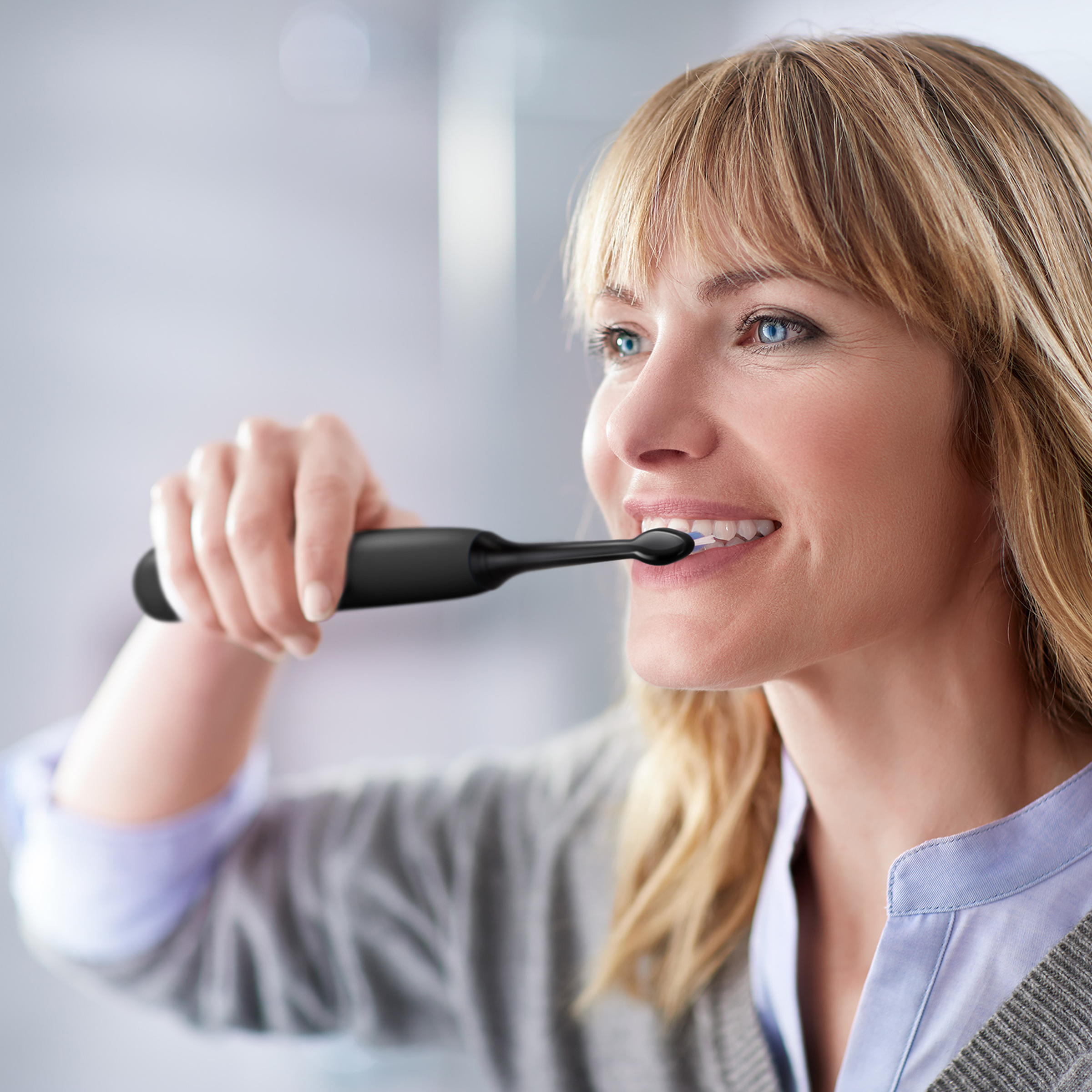 Kobieta myjąca zęby czarną elektryczną szczoteczką, zbliżenie.