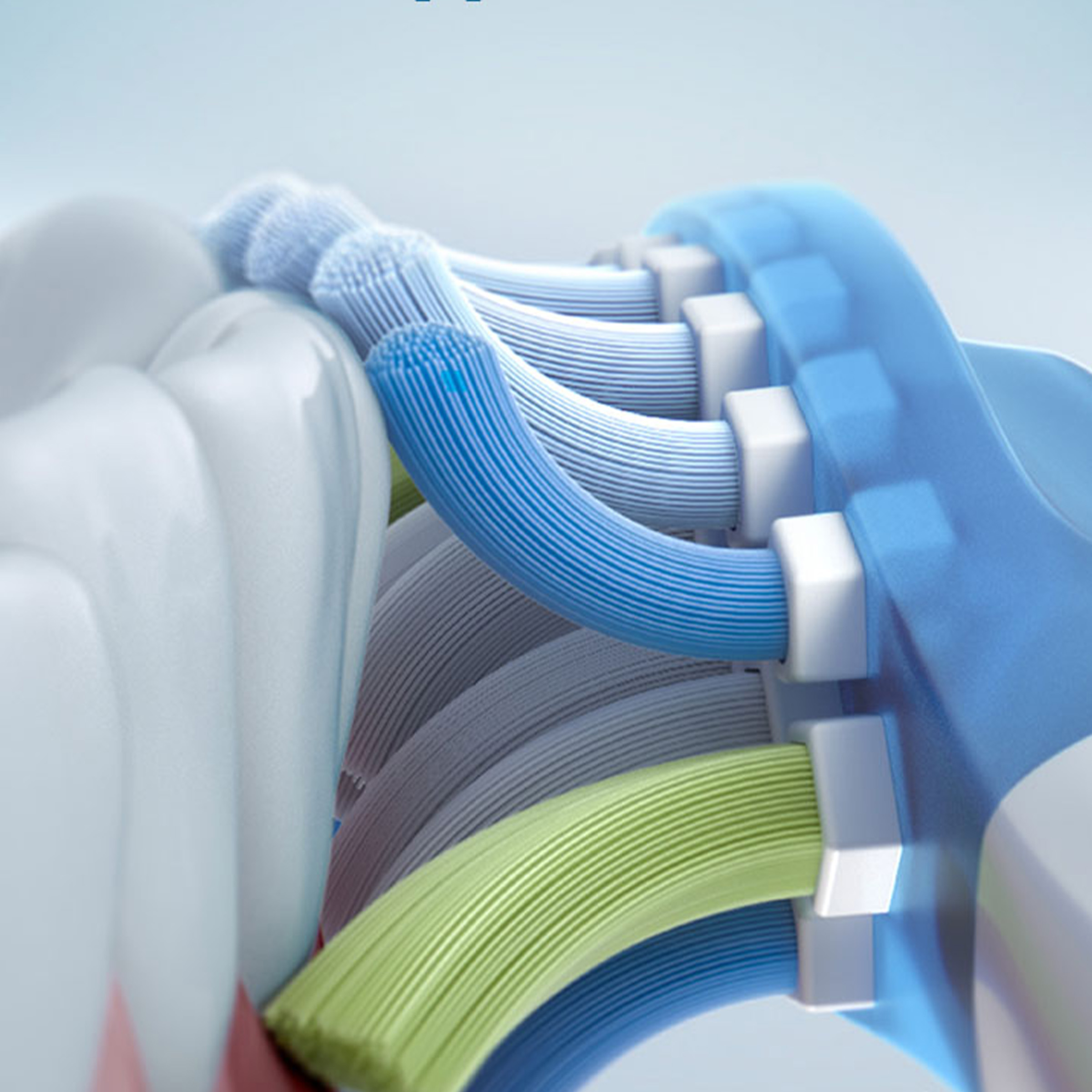 Zbliżenie główki szczoteczki do zębów z włosiem w różnych kolorach. Włosie jest niebieskie, zielone i szare.