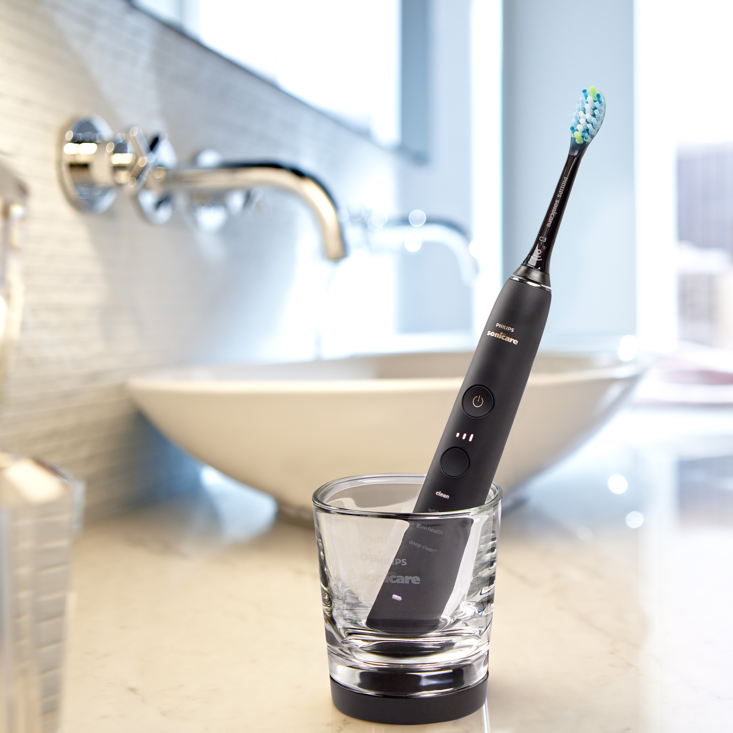 Czarna elektryczna szczoteczka do zębów w szklance na blacie łazienkowym, z umywalką w tle.