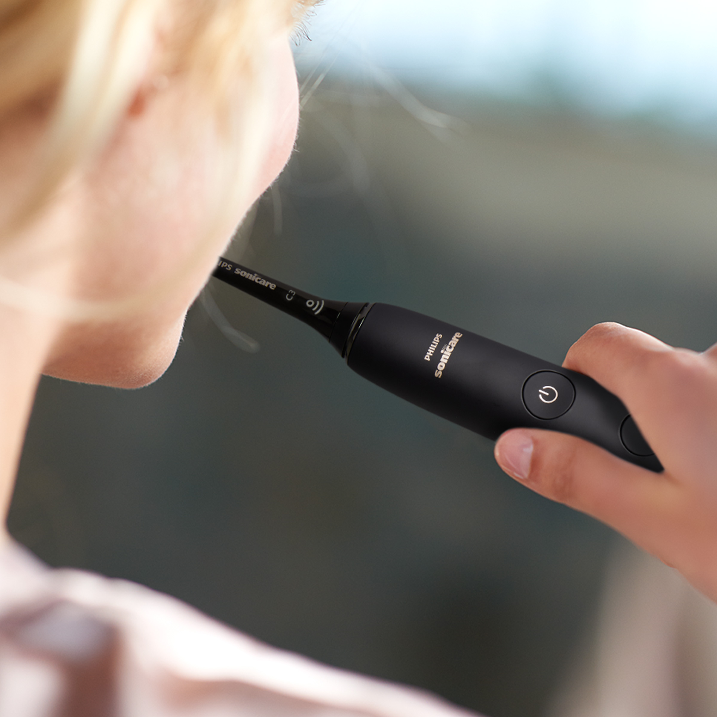 Osoba myjąca zęby czarną szczoteczką Philips Sonicare. Tło jest rozmyte.