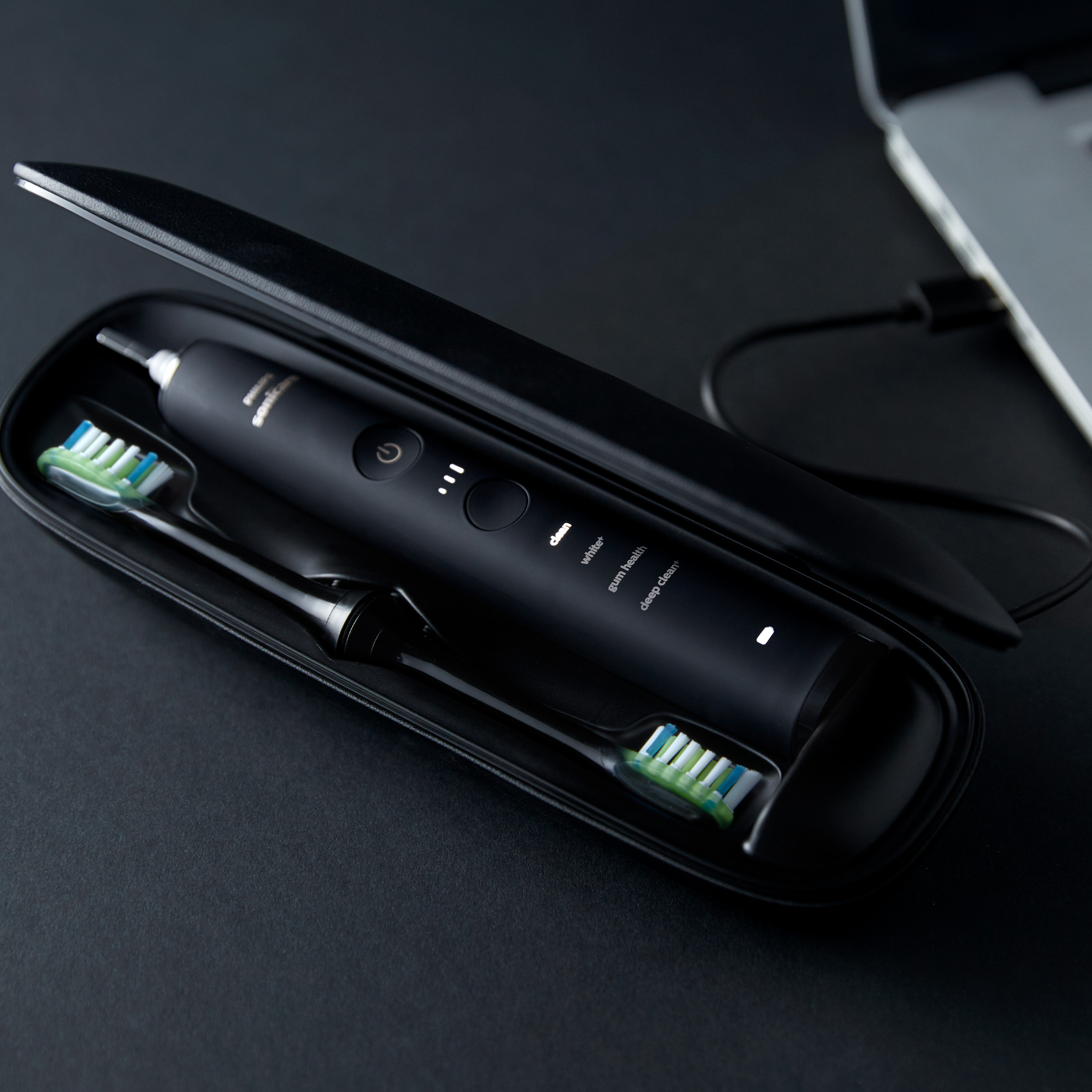 Czarna elektryczna szczoteczka do zębów i dwie końcówki w czarnym etui na ciemnej powierzchni.