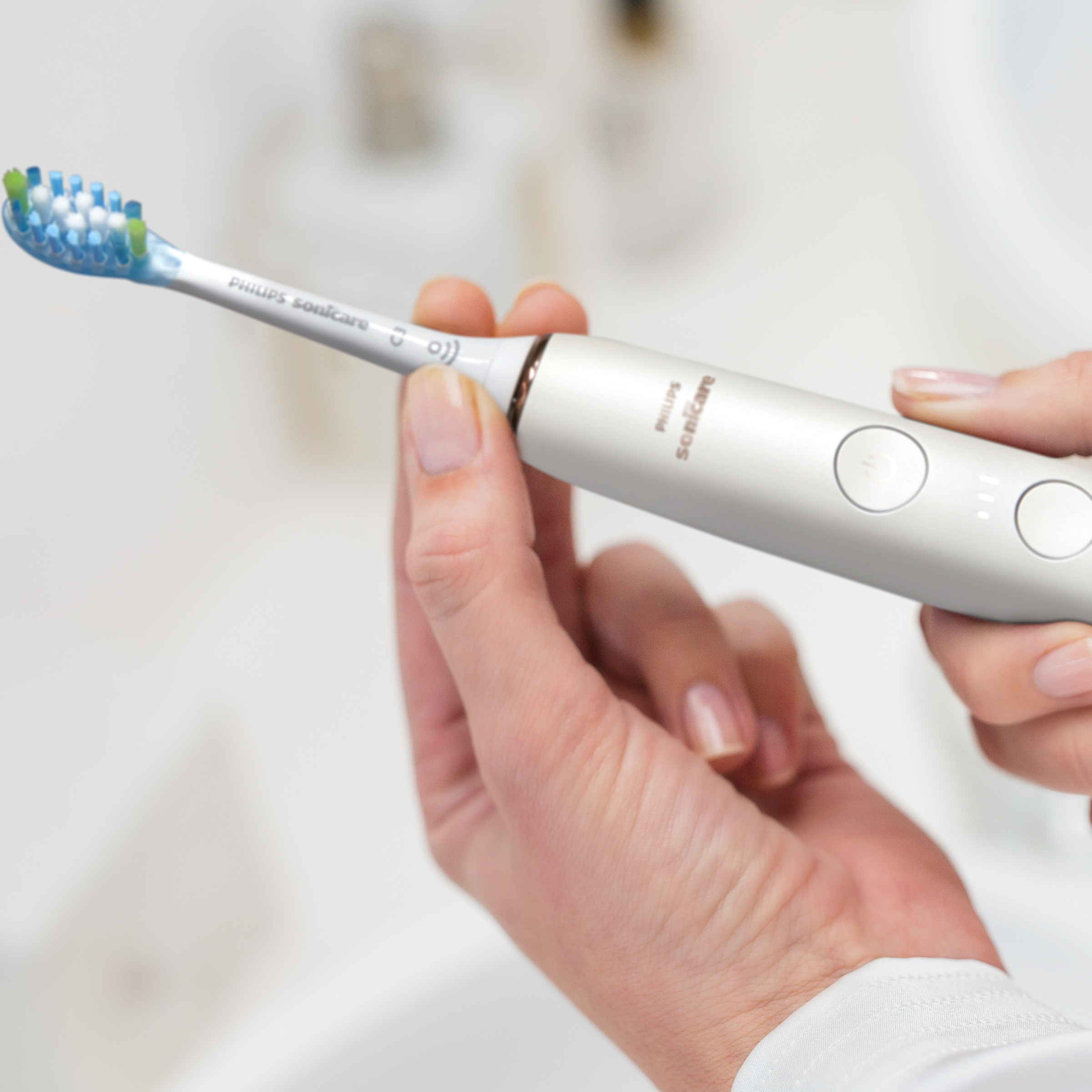 Ręka trzymająca elektryczną szczoteczkę do zębów, pokazująca włosie. Tło: łazienka.